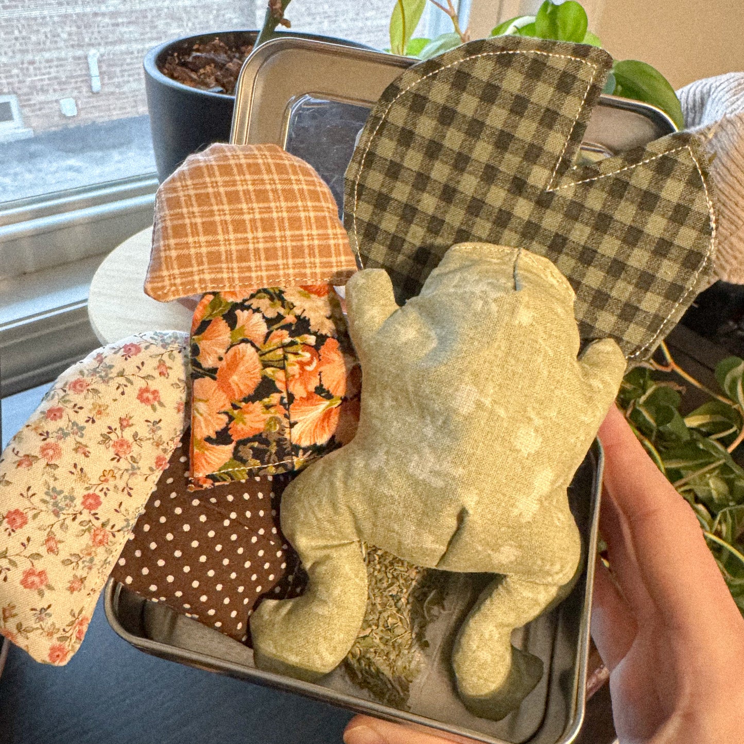 Small handmade green frog plush cat toy with patterned mushroom toys and a lily pad in a tin
