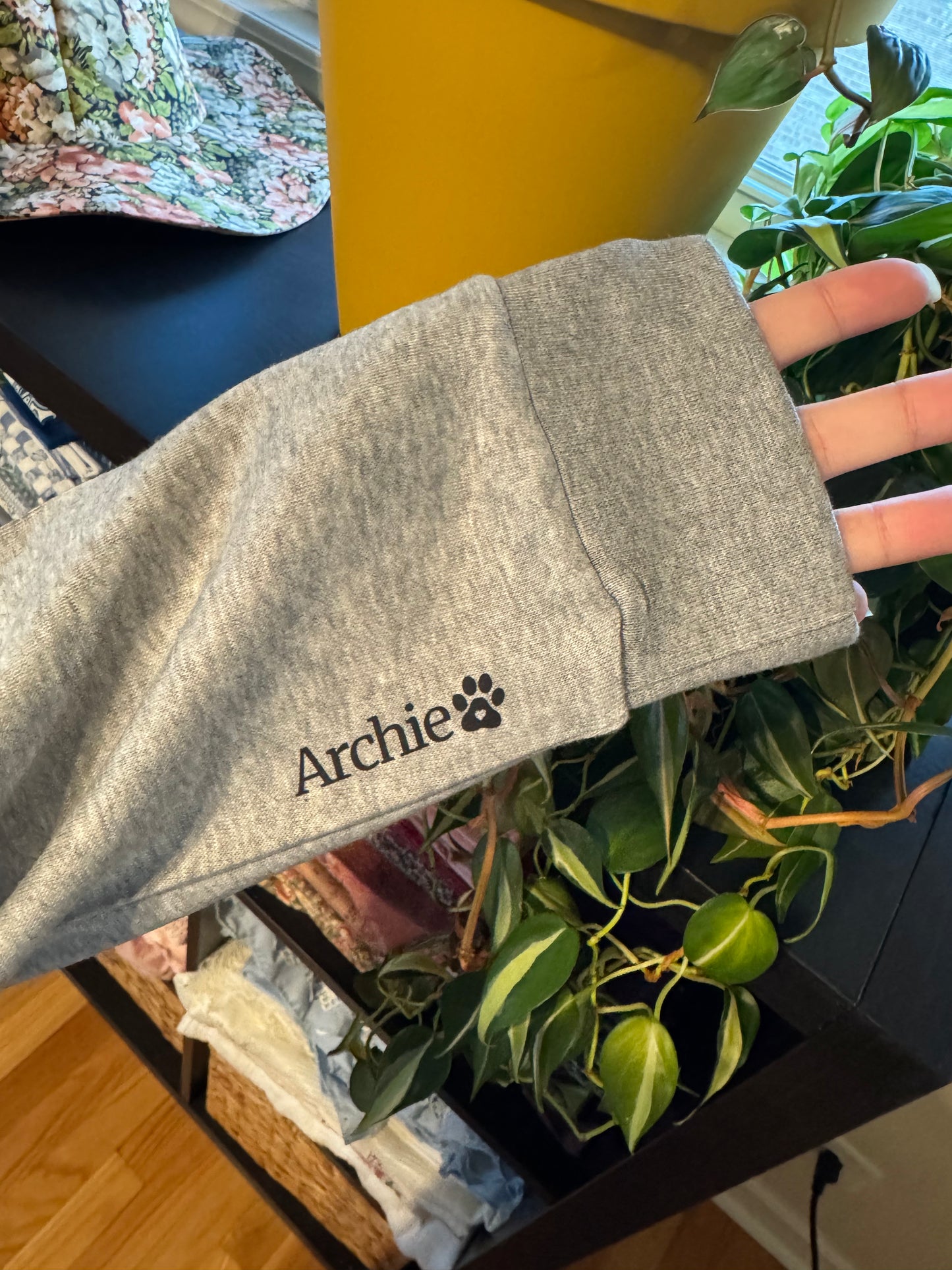 Gray pet sweater with 'Archie' and a paw print on it, held by a hand.