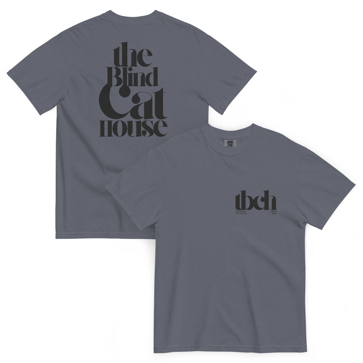 Denim colored short sleeve t-shirt shown front and back on a white background. The back features large black typography reading "The Blind Cat House" in a bold, vintage-style font The front has a small black chest logo reading "tbch" with the blind cay house" and "since 2021" beneath it
